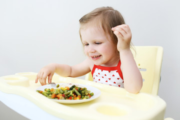Portrait of happy little 2 years girl eating fish with vegetables