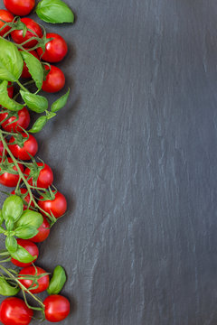 Cherry tomatoes with basil leaves on dark slate background, vertical, top view, copy space