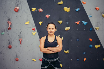 Portrait of stocky athletic brunette female climber in black outfit with protective gear over artificial painted rock background.