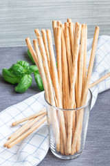 Traditional Italian snack grissini bread sticks in a glass with basil leaves on background, vertical
