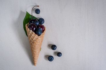 Blueberry explosion. Photo of blueberry and cherry in waffle cone on white wooden table. Top view, place for text. Berry minimalism.
