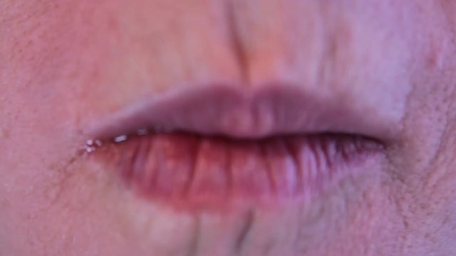 An adult woman places a nacho chip in her mouth and chews it up. Very close up of just her lips and mouth.