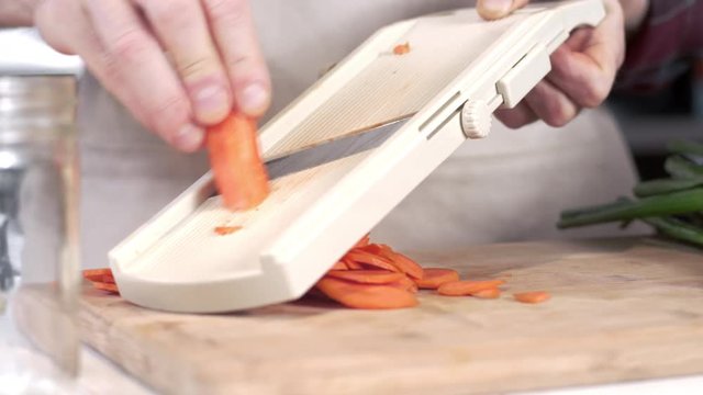 Tracking shot of chef slicing carrot using mandolin