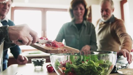Senior couple cooking dinner together with friends at home. - Powered by Adobe