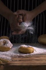 Chef 's hands sprinkling sweet donuts with icing sugar and flour sifter on background.Copy space.