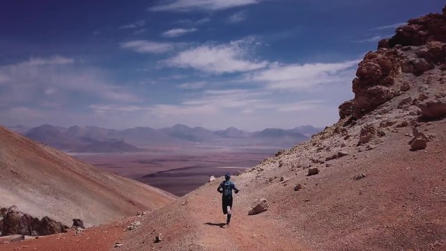 Male athlete running on the high mountain trail of the rocky desert in the Atacama desert. Aerial view, 4k