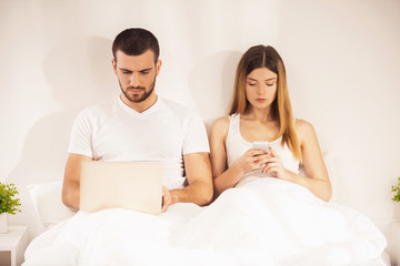 Young Couple in Bed with Smartphone and Laptop.
