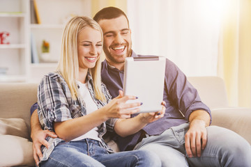 Happy Young Couple Watching into Tablet at Home.