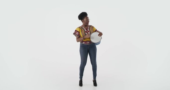 Full-height shot young African female musician playing on djembe bongo drum.
