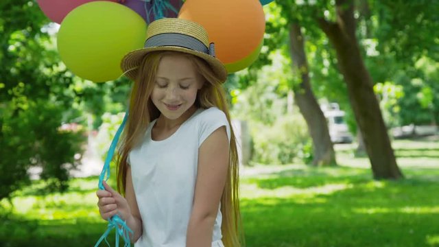 Portrait of pretty girl poses at camera with colourful balloons in sunny park