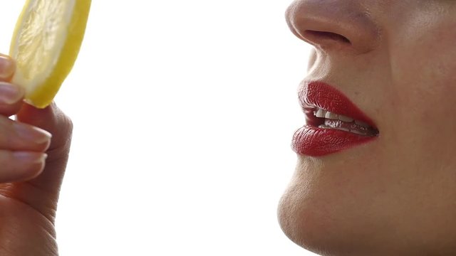 woman licks and eating juicy lemon, close-up lips on a white background. slow motion
