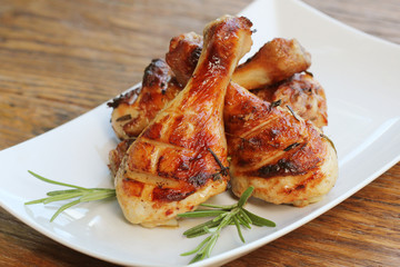 Grilled chicken legs with rosemary served on white plate. Dinner background
