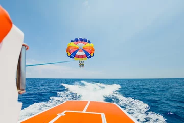 Papier Peint photo Lavable Sports nautique Personnes volant sur un parachute coloré remorqué par un bateau à moteur