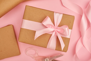 Pink satin ribbon and scissors near present box on pink flatlay