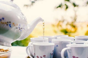 Outdoor tea party preparation. Pouring from a rustic style tea pot.