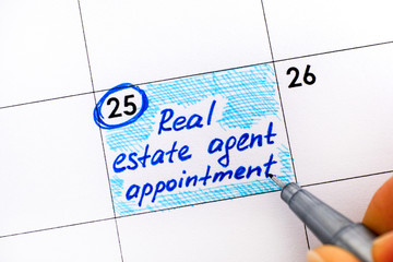 Woman fingers with pen writing reminder Real Estate Agent Appointment in calendar.