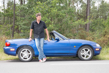pround man standing near cabriolet blue car on road