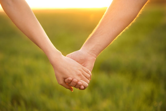 Young lovely couple holding hands in green field, closeup