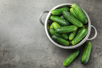 Colander with ripe fresh cucumbers on table, top view