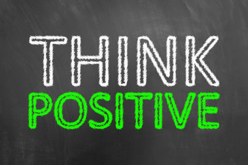 Think positive chalk text on blackboard or chalkboard.