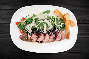 Grilled duck meat and spinach leaves in white plate on black wood background.