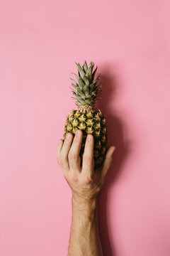 Man hand holding ripe pineapple on faded rosy background isolated. Minimalist style trendy tropical food concept.