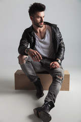 seated handsome man wearing black leather jacket looks to side