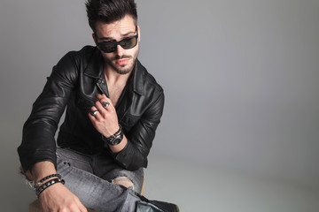 Fototapeta premium seated man wearing sunglasses and leather jacket looks to side