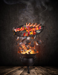 Kettle grill with hot briquettes, cast iron grate and tasty skewers flying in the air.