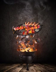 Papier Peint photo autocollant Grill / Barbecue Grille de bouilloire avec briquettes chaudes, grille en fonte et brochettes savoureuses volant dans les airs.