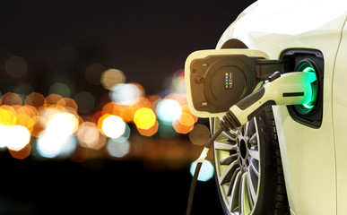 EV Car or Electric car at charging station with power supply plugged in on blurred car light on a...