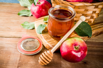 Jewish holiday Rosh Hashanah or apple feast day concept, with red apples, apple leaves and honey in jar, light blue and wooden background copy space