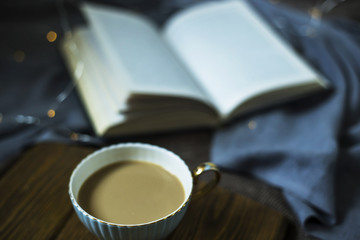A cup of coffee with milk and a book on cozy domestic plohad. Time for rest in autumn or winter