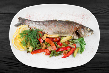 Grilled fish with vegetables on the white plate.