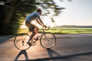 Fototapeta premium Rennradfaher im Sommer bei Sonnenuntergang