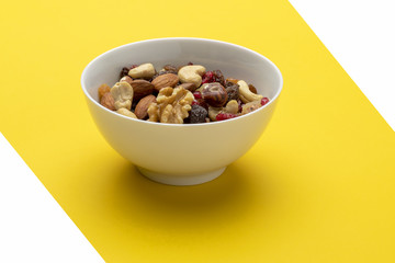 Mix of dried fruits and nuts in a bowl on a yellow background