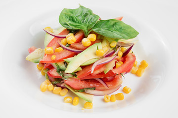 Vegetable salad with avocado, tomatoes and corn on white plate. Close-up