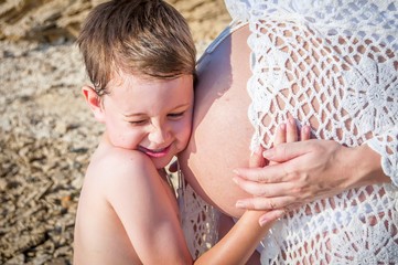 Cute sweet Caucasian child listening to his pregnant mother's belly expecting baby shaking in the...