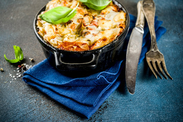 Traditional italian food, homemade lasagna with fresh basil, dark blue background copy space