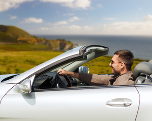 road trip, travel and people concept - happy man driving convertible car over big sur coast of california background