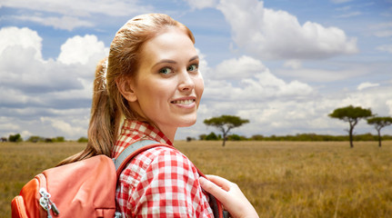 adventure, travel, tourism, hike and people concept - smiling young woman with backpack over african savannah background