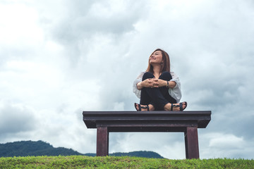 A happy asian woman sitting on a wooden bench in the park with blue sky background