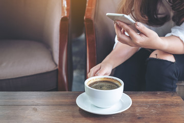 Closeup image of a woman holding , using and touching a smart phone while drinking coffee in cafe