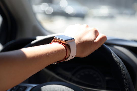 lady drives a car with one hand with a  smart watch on it