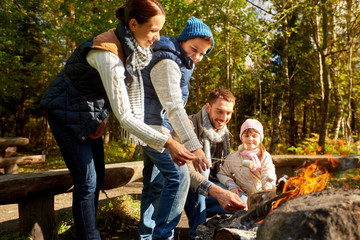 camping, travel, tourism, hike and people concept - happy family roasting marshmallow over campfire