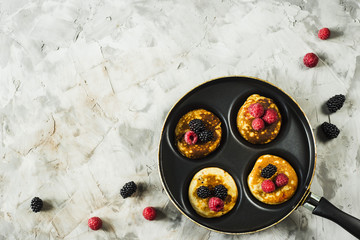 Pan with pancakes and raspberries and blackberries on a gray table. Top view, flat lay, copy space