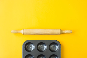 A metal mold for baking cupcakes next to a rolling pin on a yellow background. Minimalism. Top view, flat lay