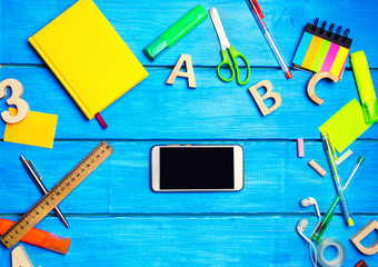 school supplies in the school desk with a phone in the center, stationery, school concept, blue background, creative chaos, markers, pens, notepads, stickers