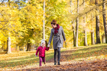Fototapeta na wymiar family, season and people concept - happy mother and little daughter walking along autumn park