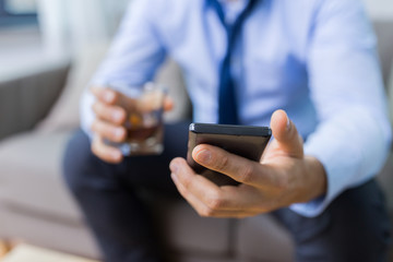 alcoholism, alcohol addiction and technology concept - close up of male hands with smartphone and glass at home